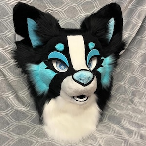 May include: A black and white furry animal head with blue accents. The head has a white muzzle and a black nose. The eyes are blue with black pupils. The head is made of soft, plush fabric.