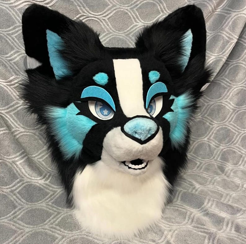 May include: A black and white furry animal head with blue accents. The head has a white muzzle and a black nose. The eyes are blue with black pupils. The head is made of soft, plush fabric.