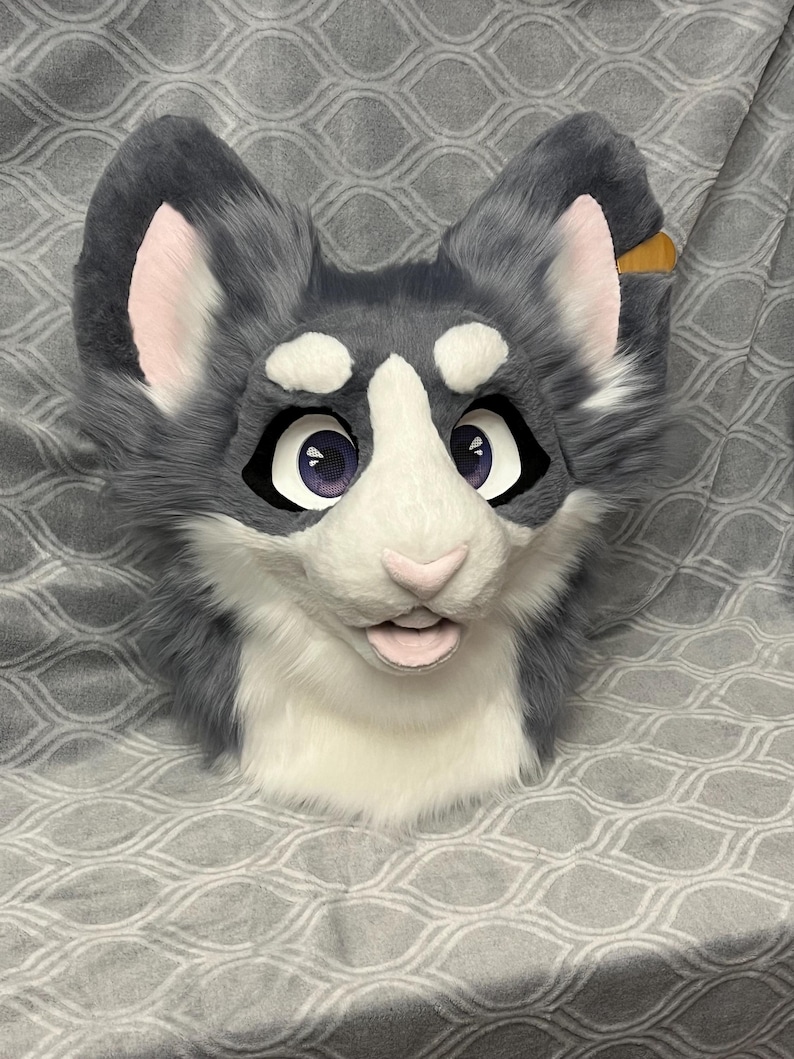 May include: A gray and white furry animal head with large ears, black eyes, and a pink nose. The head is made of plush fabric and has a realistic appearance.
