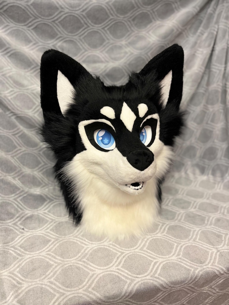 May include: A black and white furry wolf head with blue eyes. The wolf head is a plush toy and is made to look realistic.