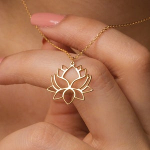 May include: A gold chain necklace with a delicate lotus flower pendant. The pendant is made of a thin metal and has a cutout design.