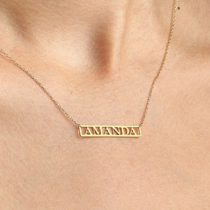 May include: A gold necklace with a rectangular pendant that says "AMANDA" in a cutout font.