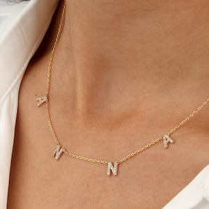 May include: A gold chain necklace with four small, diamond-encrusted letters spelling out the name "ANNA".