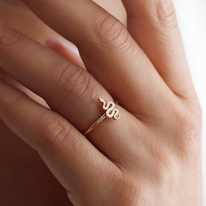 May include: A gold ring with a snake design. The ring is on a person's finger.
