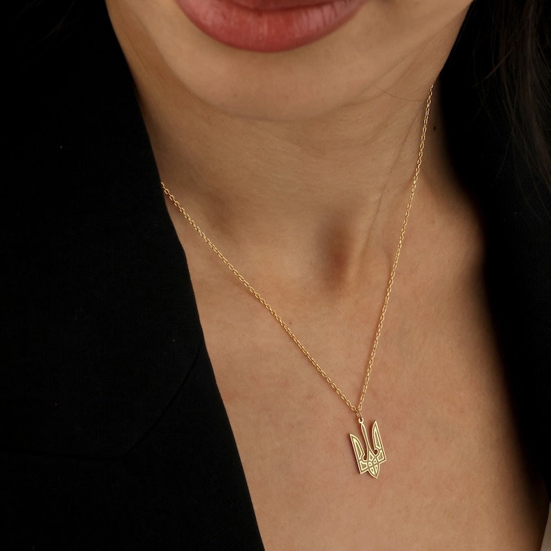 May include: A gold chain necklace with a small, detailed trident pendant. The pendant is a symbol of Ukraine.