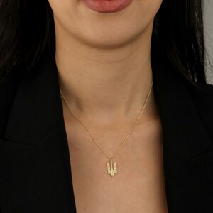 May include: A gold necklace with a trident pendant. The pendant is a stylized version of the Ukrainian coat of arms.