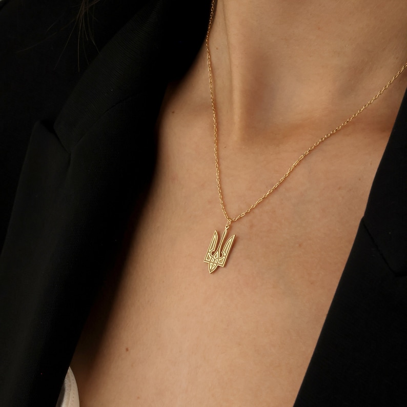May include: A gold chain necklace with a pendant featuring the Ukrainian trident symbol.