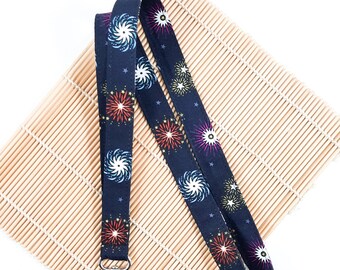 May include: A black lanyard with a colorful firework pattern. The lanyard has a silver metal clip.
