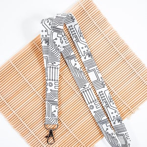 May include: White lanyard with a black circuit board pattern. The lanyard has a silver metal clip.