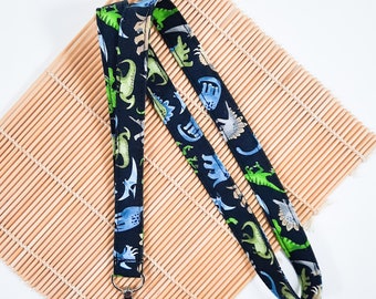 May include: A black lanyard with a dinosaur print. The lanyard has a silver clip on one end.