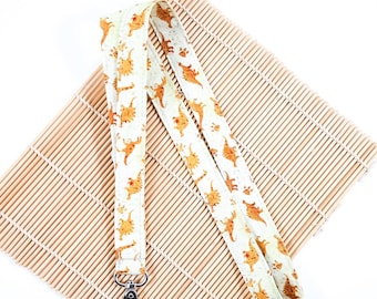 May include: White lanyard with a brown dinosaur print and a silver clip. The lanyard is lying on a bamboo mat.