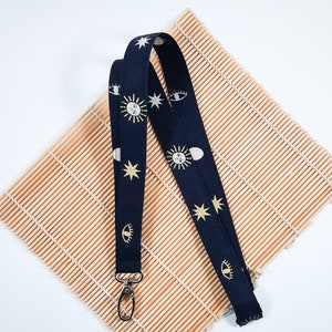 May include: A navy blue lanyard with a gold and white pattern of eyes, moons, and stars. The lanyard has a silver metal clasp.