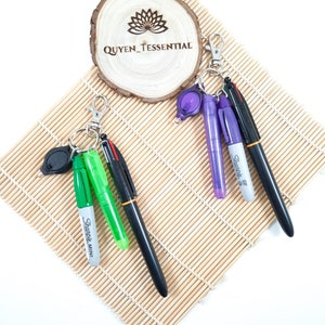 May include: A keychain with a black pen, a green highlighter, a silver Sharpie Mini marker, and a purple Sharpie marker. The keychain also has a small black light.