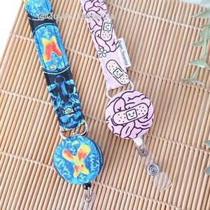 May include: Two lanyards with retractable badge reels. One is black with blue and yellow brain scan images. The other is light pink with brain and bandage graphics. Both have clear plastic badge holders.