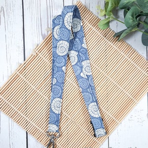 May include: A blue and white patterned lanyard with a silver swivel clip. The lanyard has a repeating pattern of seashells.