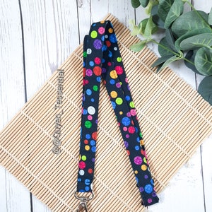 May include: A black lanyard with a colorful polka dot pattern. The lanyard has a silver swivel clip.
