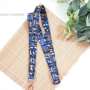 Könnte beinhalten: Ein blaues und goldenes Lanyard mit einem ägyptischen Hieroglyphenmuster. Das Lanyard hat einen goldenen Metallverschluss.