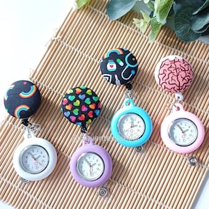 Peut inclure: Six montres de poche d'infirmière avec des dessus à motifs, dont des arcs-en-ciel, des cœurs et des symboles médicaux. Les montres ont des cadrans blancs avec des chiffres et des aiguilles noirs, et sont de couleurs comme le bleu, le rose et le violet.