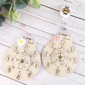 May include: Two wooden baby position reference wheels with a flower and a bee charm. The wheels are labeled "Sarah" and "Laurer" and show different baby positions in the womb.