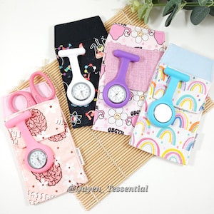 May include: Several nurse fob watches in pink, purple, white, and blue, each with a different patterned fabric holder. The patterns include brains, flowers, and rainbows. A pair of pink scissors is also present in the image.