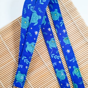 May include: Two blue fabric straps with a repeating pattern of sea turtles, leaves, and stars. The straps are on a bamboo mat.