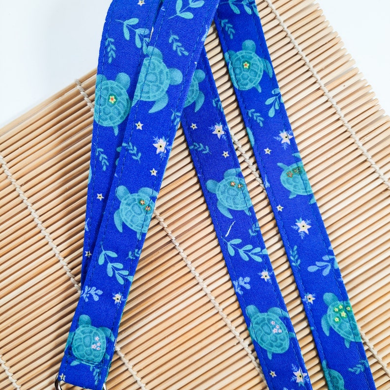 May include: Two blue fabric straps with a repeating pattern of sea turtles, leaves, and stars. The straps are on a bamboo mat.