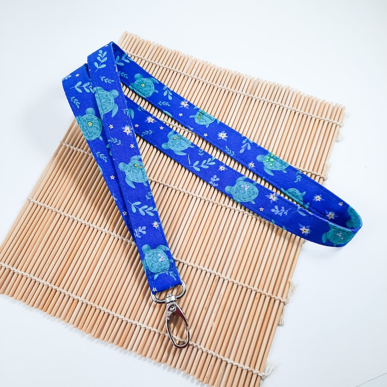 May include: A blue lanyard with a pattern of sea turtles and flowers. The lanyard has a silver swivel clasp.