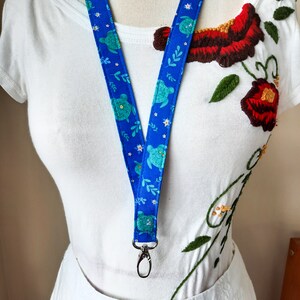 May include: A blue lanyard with a white background and a pattern of green sea turtles and white flowers. The lanyard has a silver clip at the end.
