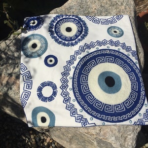 May include: White throw pillow with blue and white embroidered evil eye designs and Greek key patterns.