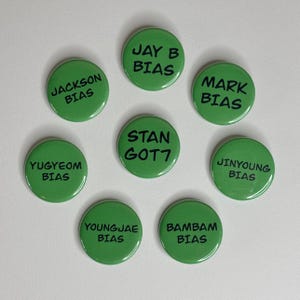 May include: A collection of eight green round buttons. Each button has black text. The text on the buttons includes the words "JACKSON BIAS", "JAY B BIAS", "MARK BIAS", "YUGYEOM BIAS", "STAN GOT7", "JINYOUNG BIAS", "YOUNGJAE BIAS", and "BAMBAM BIAS".