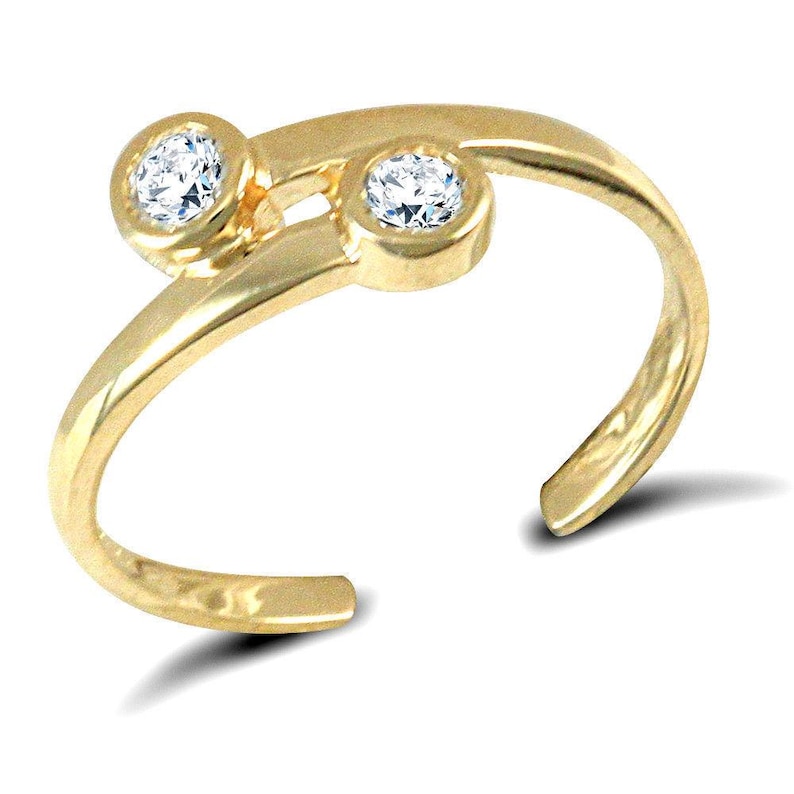 Pu&ograve; includere: Un anello per il piede color oro con due pietre preziose rotonde e trasparenti. L'anello ha un design aperto e fluido, con le pietre preziose incastonate in castoni a lunetta. L'anello &egrave; curvo per adattarsi al piede.