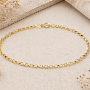Peut inclure: Un bracelet chaîne doré avec un design à maillons circulaires. Le bracelet est présenté sur une surface de ton neutre, avec des fleurs séchées et un arrière-plan texturé. Le bracelet est sécurisé par un fermoir.