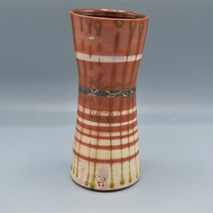 May include: A brown ceramic vase with a white and green striped pattern. The vase has a narrow neck and a wide base. It is decorated with a black and white drawing of two birds. The vase is signed with a green stamp.