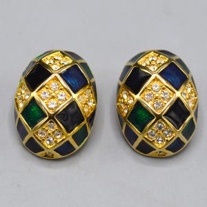 May include: A pair of oval-shaped earrings with a gold-tone setting. The earrings feature a geometric pattern of black, blue, and green enamel squares, accented with clear crystals. The design is reminiscent of a mosaic.