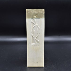 May include: White ceramic vase with an embossed design of a dragonfly and a circle. The vase has a textured surface and a slightly off-white color.
