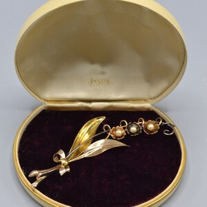 May include: A gold and silver lily of the valley brooch with pearl accents, in a cream-colored velvet lined box with the inscription "Inson".