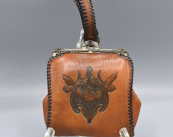 Puede incluir: Un bolso de cuero marrón con cierre de plata y asa de cuero negro. El bolso tiene un diseño floral en relieve en la parte delantera.