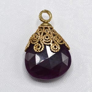 May include: A purple gemstone pendant with a gold filigree design. The pendant is shaped like a teardrop and has a delicate, intricate design.