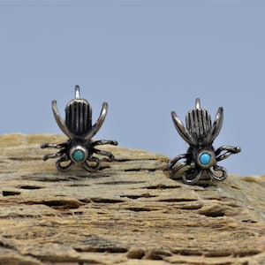 May include: A pair of silver earrings with turquoise stones in the shape of a stylized insect.