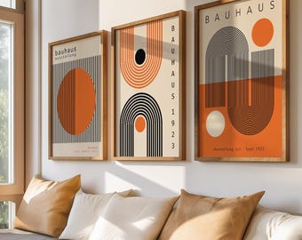 May include: Three framed Bauhaus art prints with geometric designs in orange, black, and cream colors. The prints are displayed above a built-in bench with pillows in shades of beige and tan. The room has a large window and hardwood floors.