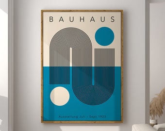 May include: A framed Bauhaus art print. The artwork features a geometric design with black lines, a blue circle, and a beige background. The lower half is blue, and the text "BAUHAUS" is at the top. The print is in a room with a window and a brown stool.