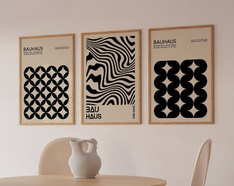 May include: Three framed black and white geometric prints with the text "BAUHAUS" on a beige wall above a wooden table with a white ceramic vase and four beige chairs.