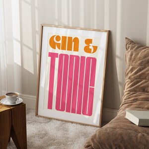 May include: A framed print with the text "Gin & Tonic" in a retro, bold font. The text is in orange and pink on a white background.