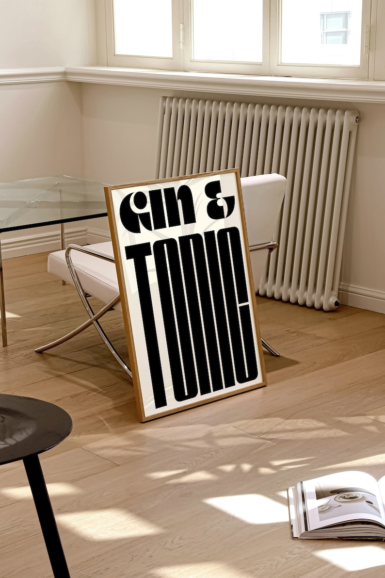 May include: A framed print with the text "Gin & Tonic" in bold, black letters on a white background. The frame is a light wood color.
