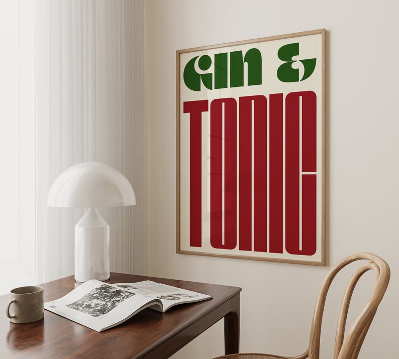 May include: A framed poster with the text "Gin & Tonic" in green and red letters on a white background. The poster is hanging on a white wall.