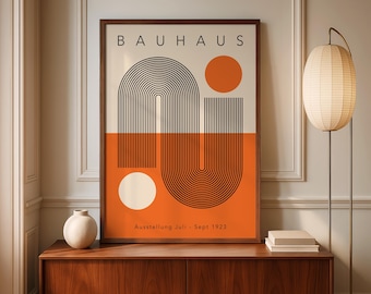 May include: A framed Bauhaus art print with a geometric design in black, orange, and cream. The print features the word "BAUHAUS" at the top and the text "Ausstellung Juli - Sept 1923" at the bottom. The artwork is displayed on a wooden cabinet.