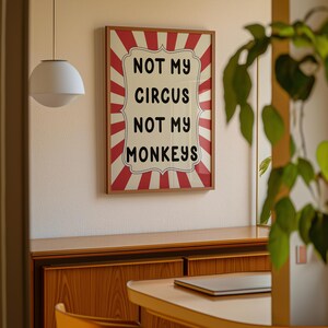 K&ouml;nnte beinhalten: Ein gerahmter Druck mit einem rot-wei&szlig; gestreiften Hintergrund und einem wei&szlig;en Banner mit dem Text "Not My Circus Not My Monkeys".