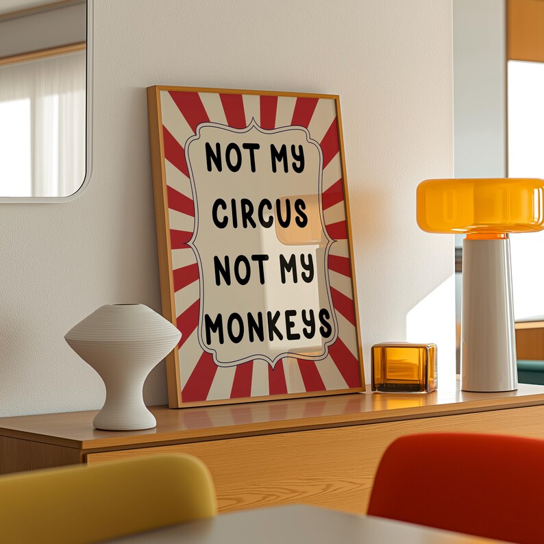 K&ouml;nnte beinhalten: Ein gerahmter Druck mit einem rot-wei&szlig; gestreiften Hintergrund und dem Text "NOT MY CIRCUS NOT MY MONKEYS" in Schwarz. Der Druck h&auml;ngt an einer wei&szlig;en Wand &uuml;ber einer Kommode aus Holz mit einer Lampe und anderen Dekorationen.
