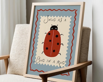 Puede incluir: Un estampado enmarcado con un diseño de mariquita roja con lunares negros, sobre un fondo crema dentro de un borde azul. El texto dice "Snug as a Bug in a Rug". La obra de arte se muestra en un marco de madera clara.
