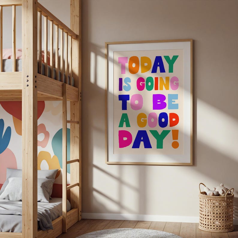 May include: A framed art print with the text "TODAY IS GOING TO BE A GOOD DAY!" in colorful, bold letters. The print is in a light wood frame and hangs on a beige wall. A wooden bunk bed and a woven basket are also visible.